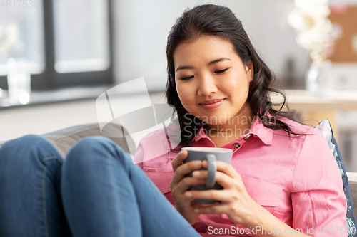 Image of smiling asian young woman drinking coffee at home