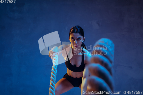 Image of Caucasian young female athlete practicing on blue studio background in neon light