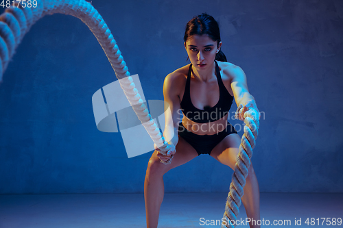 Image of Caucasian young female athlete practicing on blue studio background in neon light