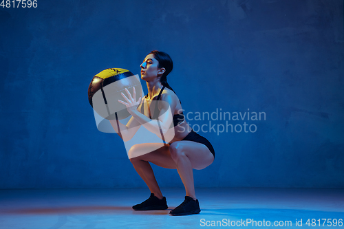 Image of Caucasian young female athlete practicing on blue studio background in neon light