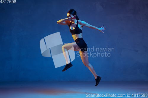 Image of Caucasian young female athlete practicing on blue studio background in neon light