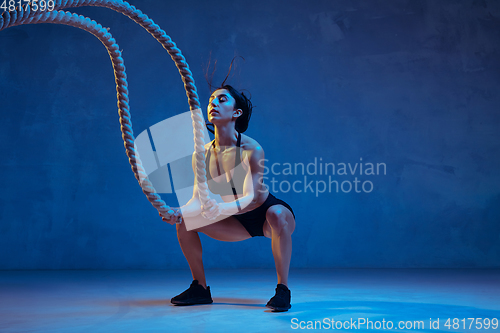 Image of Caucasian young female athlete practicing on blue studio background in neon light