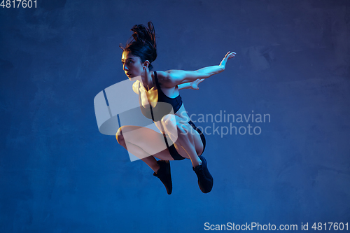 Image of Caucasian young female athlete practicing on blue studio background in neon light