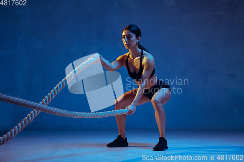 Image of Caucasian young female athlete practicing on blue studio background in neon light