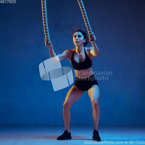 Image of Caucasian young female athlete practicing on blue studio background in neon light