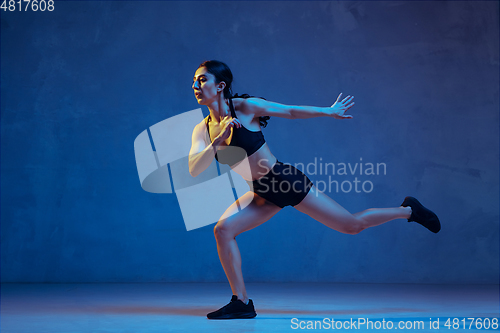 Image of Caucasian young female athlete practicing on blue studio background in neon light