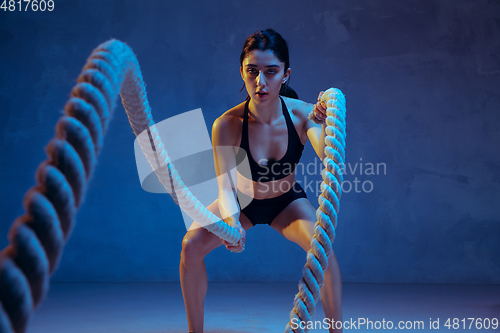 Image of Caucasian young female athlete practicing on blue studio background in neon light