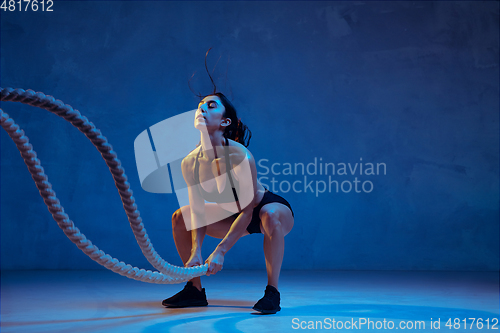 Image of Caucasian young female athlete practicing on blue studio background in neon light