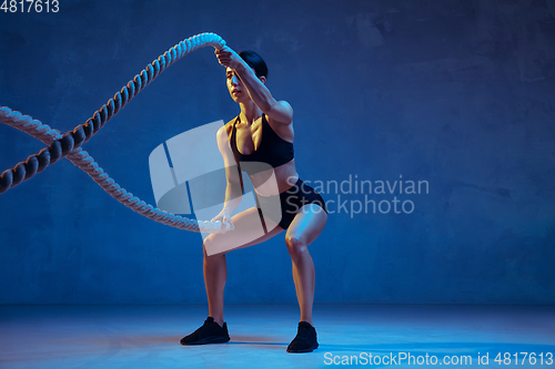 Image of Caucasian young female athlete practicing on blue studio background in neon light