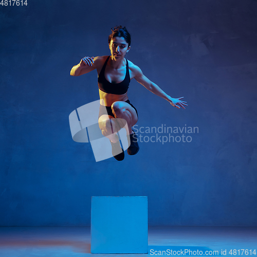 Image of Caucasian young female athlete practicing on blue studio background in neon light