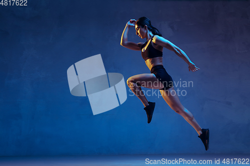 Image of Caucasian young female athlete practicing on blue studio background in neon light