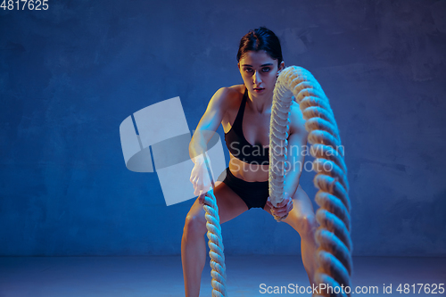 Image of Caucasian young female athlete practicing on blue studio background in neon light