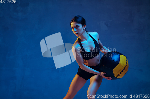 Image of Caucasian young female athlete practicing on blue studio background in neon light