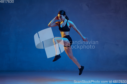 Image of Caucasian young female athlete practicing on blue studio background in neon light