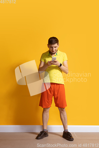 Image of Young caucasian man using smartphone. Full body length portrait isolated over yellow background.