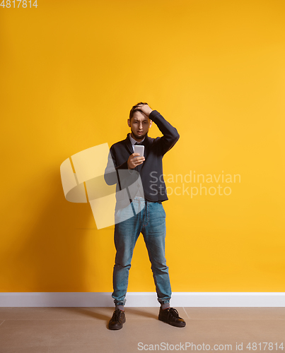 Image of Young caucasian man using smartphone. Full body length portrait isolated over yellow background.
