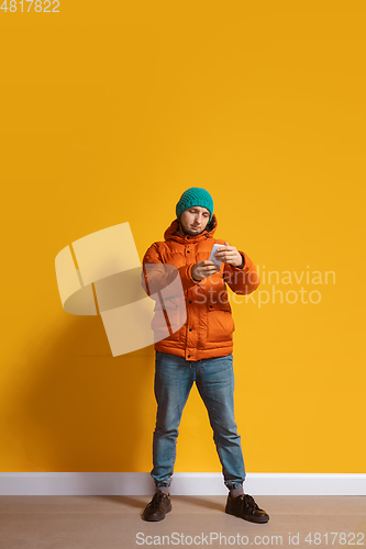 Image of Young caucasian man using smartphone. Full body length portrait isolated over yellow background.