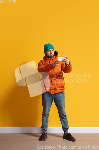 Image of Young caucasian man using smartphone. Full body length portrait isolated over yellow background.