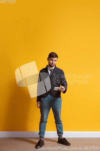 Image of Young caucasian man using smartphone. Full body length portrait isolated over yellow background.