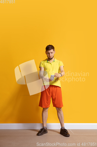 Image of Young caucasian man using smartphone. Full body length portrait isolated over yellow background.