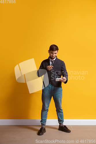 Image of Young caucasian man using smartphone. Full body length portrait isolated over yellow background.