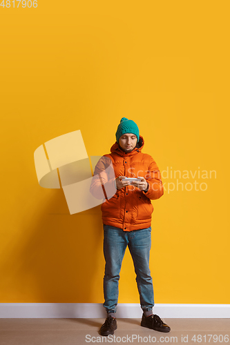 Image of Young caucasian man using smartphone. Full body length portrait isolated over yellow background.