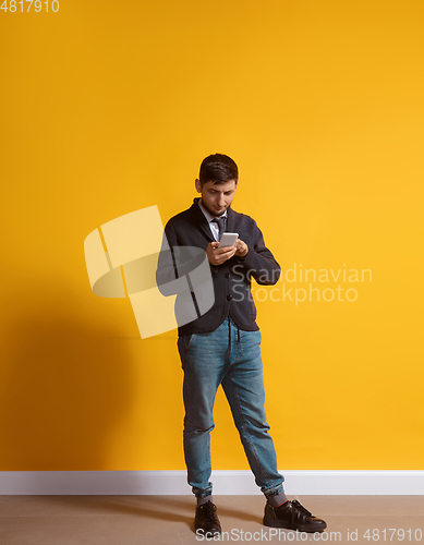 Image of Young caucasian man using smartphone. Full body length portrait isolated over yellow background.