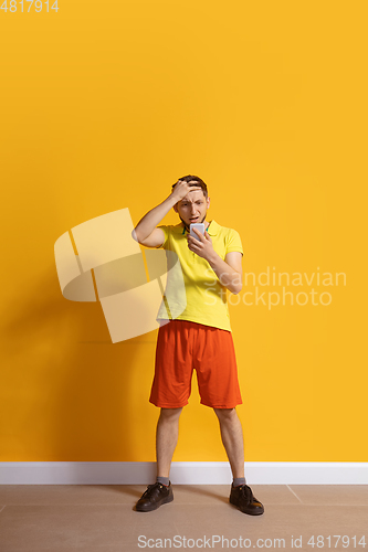 Image of Young caucasian man using smartphone. Full body length portrait isolated over yellow background.