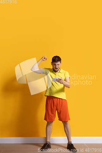 Image of Young caucasian man using smartphone. Full body length portrait isolated over yellow background.