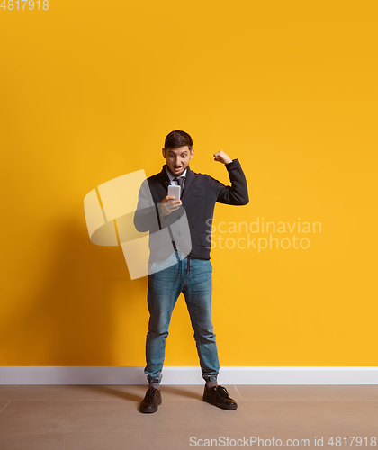 Image of Young caucasian man using smartphone. Full body length portrait isolated over yellow background.