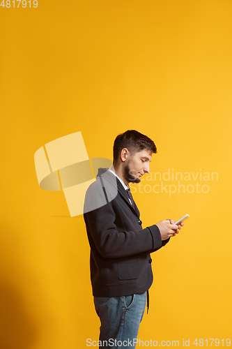 Image of Young caucasian man using smartphone. Full body length portrait isolated over yellow background.