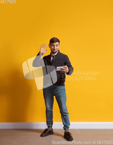 Image of Young caucasian man using smartphone. Full body length portrait isolated over yellow background.