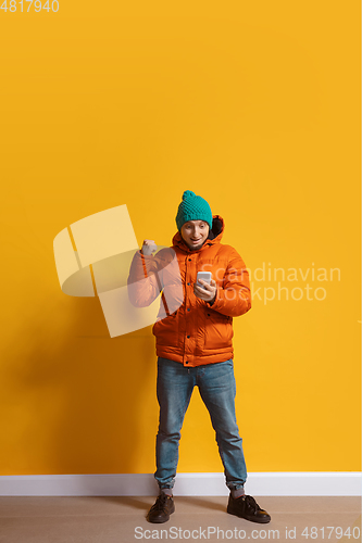 Image of Young caucasian man using smartphone. Full body length portrait isolated over yellow background.