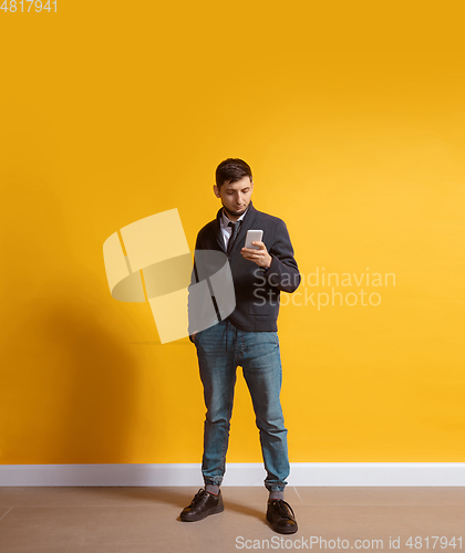 Image of Young caucasian man using smartphone. Full body length portrait isolated over yellow background.