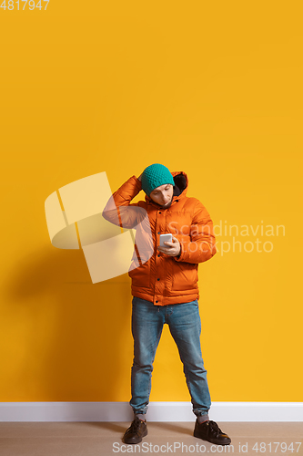Image of Young caucasian man using smartphone. Full body length portrait isolated over yellow background.