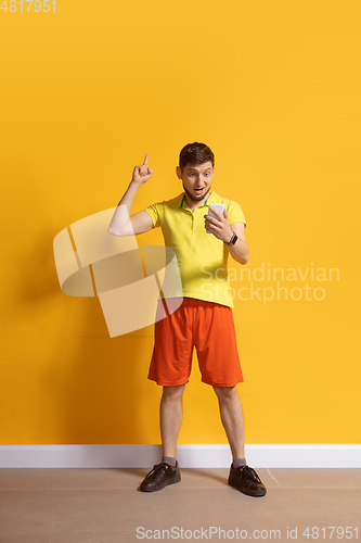 Image of Young caucasian man using smartphone. Full body length portrait isolated over yellow background.