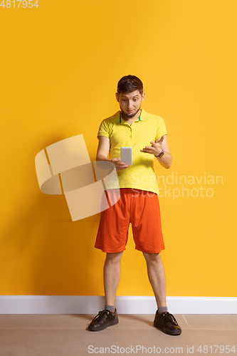 Image of Young caucasian man using smartphone. Full body length portrait isolated over yellow background.