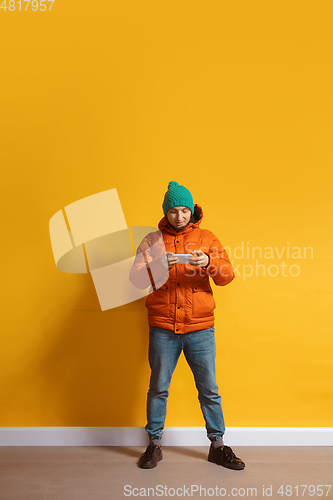 Image of Young caucasian man using smartphone. Full body length portrait isolated over yellow background.