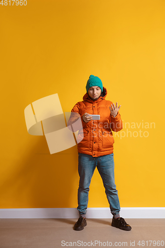 Image of Young caucasian man using smartphone. Full body length portrait isolated over yellow background.