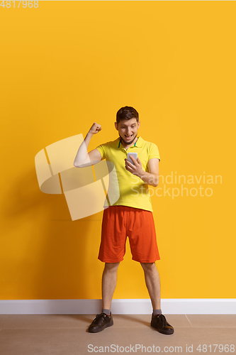 Image of Young caucasian man using smartphone. Full body length portrait isolated over yellow background.