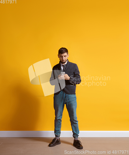 Image of Young caucasian man using smartphone. Full body length portrait isolated over yellow background.