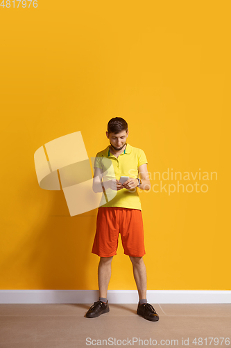 Image of Young caucasian man using smartphone. Full body length portrait isolated over yellow background.