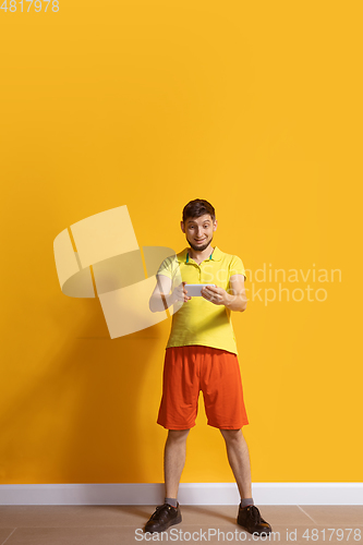 Image of Young caucasian man using smartphone. Full body length portrait isolated over yellow background.