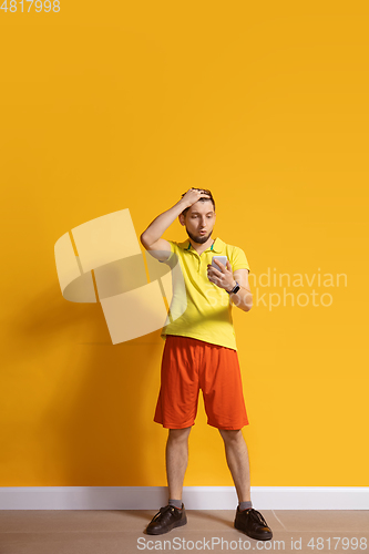 Image of Young caucasian man using smartphone. Full body length portrait isolated over yellow background.