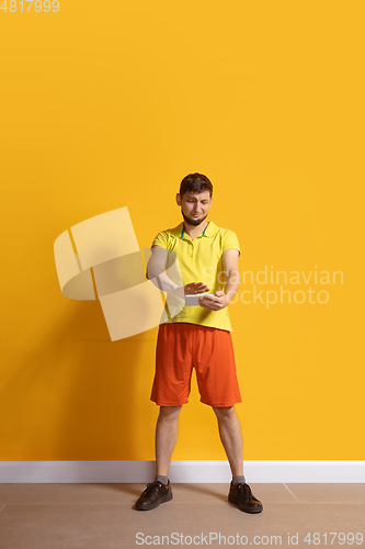 Image of Young caucasian man using smartphone. Full body length portrait isolated over yellow background.
