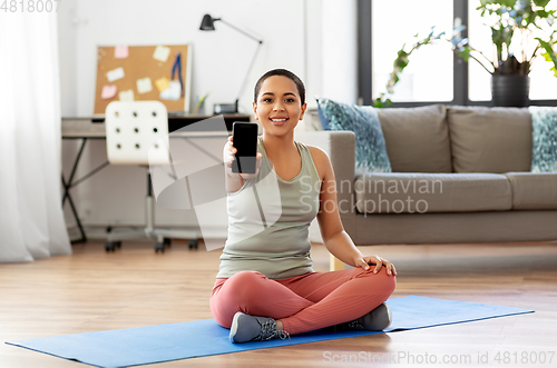 Image of woman with smartphone sits on exercise mat at home