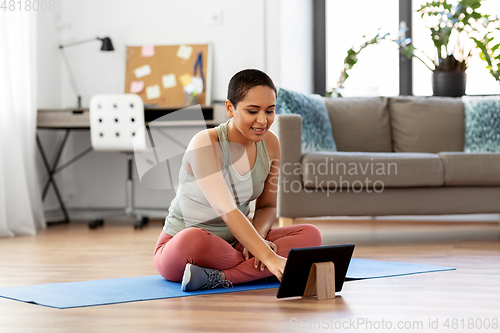 Image of woman with tablet pc sits on exercise mat at home