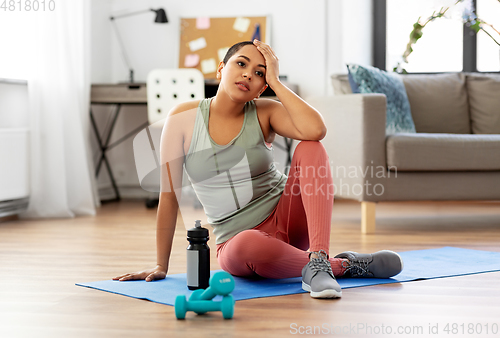 Image of tired woman with bottle and dumbbells at home