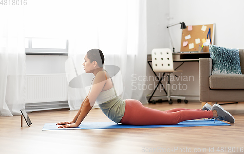 Image of woman with tablet pc doing yoga cobra pose at home