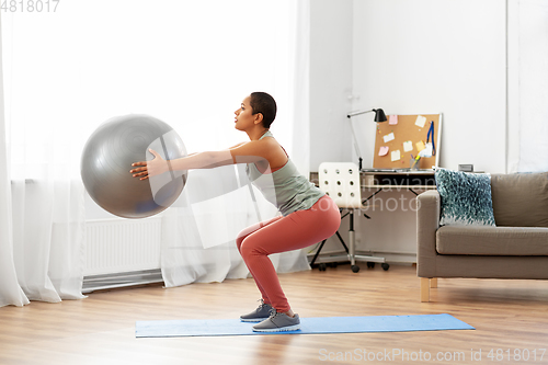 Image of woman doing squats with fitness ball at home